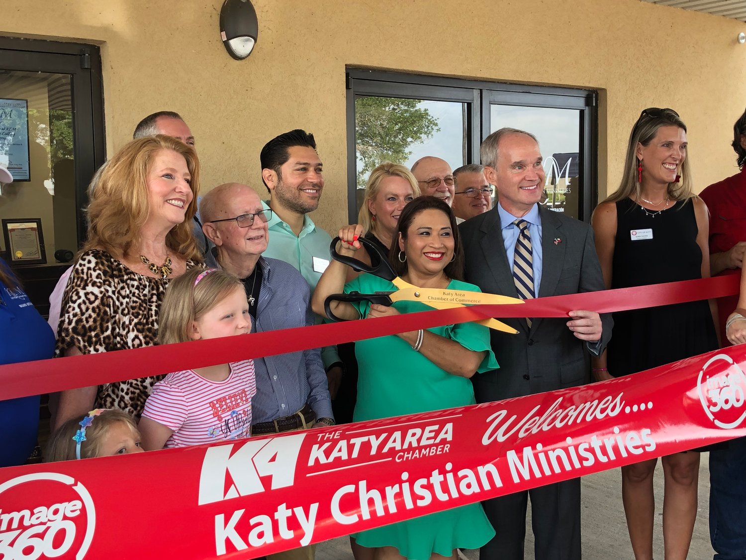 Deysi Crespo, Katy Christian Ministries executive director, prepares to cut the ceremonial ribbon provided by the Katy Area Chamber of Commerce. KCM Board parliamentarian and past president Patty Lacy stands at left. State Rep. Mike Schofield, R-Houston, and Katy Ward B Council Member Gina Hicks stand at Crespo’s left.