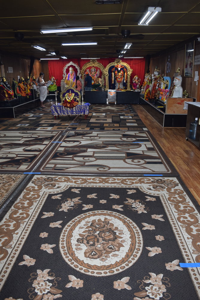 Hindu worshipers pray while a monk reads at Sai Durga Shiva Vishnu Mandir. The floor of the temple, which usually has more followers during prayer times, is marked with blue painters tape to ensure worshipers can maintain a safe social distance from one another.