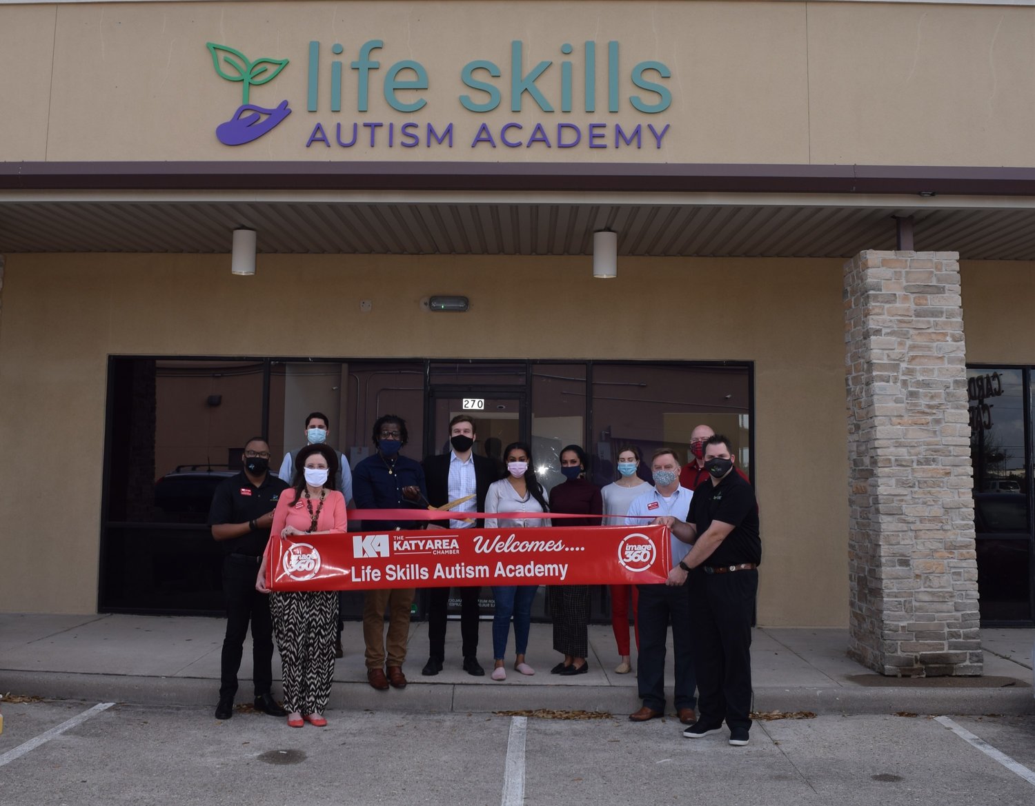 Dehazard Allen (center with scissors), clinical director of Life Skills Autism Academy in Katy is joined by Life Skills Autism Academy program director Nathan Rabens (behind scissors) and members of the Katy Area Chamber of Commerce and other academy staff for the autism clinic’s March 9 ribbon cutting.