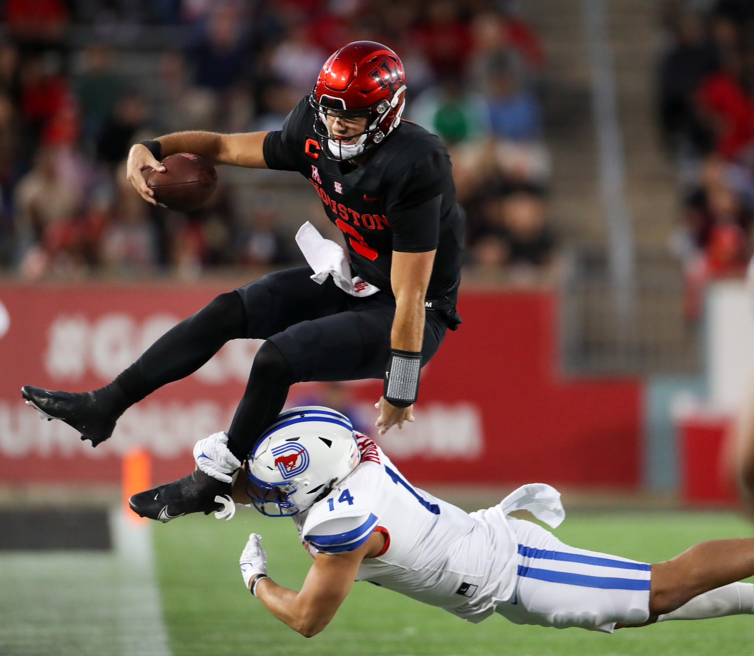 Houston Cougars quarterback Clayton Tune (3) leaps in an attempt to avoid the tackle attempt of SMU Mustangs linebacker Richard Moore (14) during an NCAA football game between Houston and SMU on October 30, 2021 in Houston, Texas.