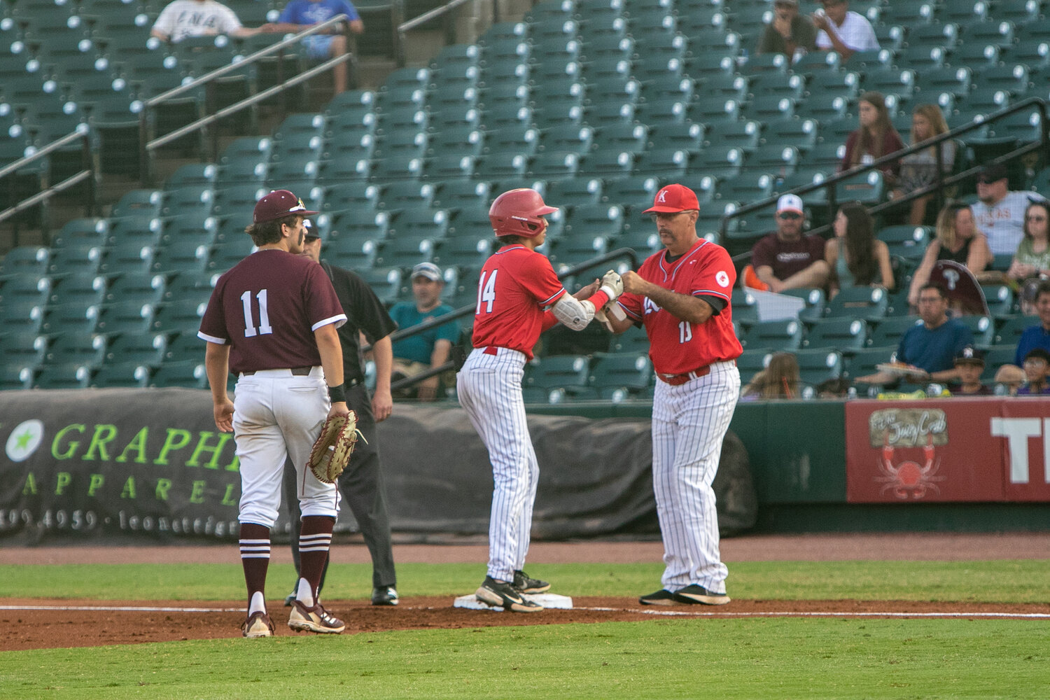 AJ Atkinson fist bumps first base coach Michael Langan during Friday's Regional Final between Katy and Pearland at Constellation Field in Sugar Land.